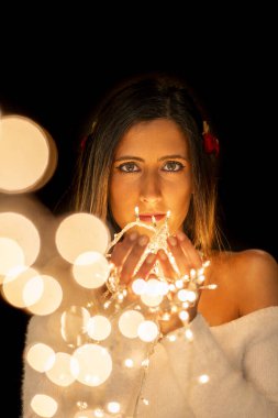 Genç bir kadın farklı pozlarda siyah bir arkaplanda Noel 'in sicim ışıklarını tutuyor..