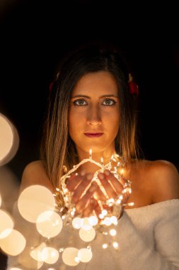 Genç bir kadın farklı pozlarda siyah bir arkaplanda Noel 'in sicim ışıklarını tutuyor..