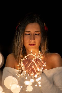 Genç bir kadın farklı pozlarda siyah bir arkaplanda Noel 'in sicim ışıklarını tutuyor..