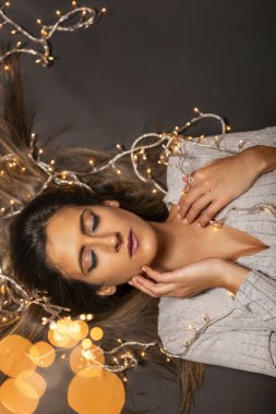 Genç bir kadın farklı pozlarda siyah bir arkaplanda Noel 'in sicim ışıklarını tutuyor..