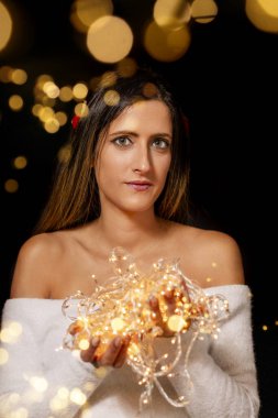 Genç bir kadın farklı pozlarda siyah bir arkaplanda Noel 'in sicim ışıklarını tutuyor..