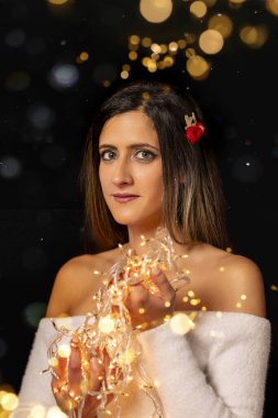 Genç bir kadın farklı pozlarda siyah bir arkaplanda Noel 'in sicim ışıklarını tutuyor..