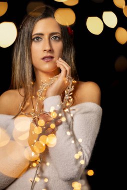 Genç bir kadın farklı pozlarda siyah bir arkaplanda Noel 'in sicim ışıklarını tutuyor..