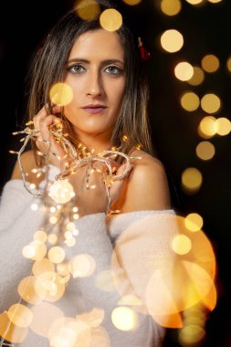 Genç bir kadın farklı pozlarda siyah bir arkaplanda Noel 'in sicim ışıklarını tutuyor..