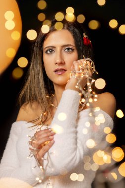 Genç bir kadın farklı pozlarda siyah bir arkaplanda Noel 'in sicim ışıklarını tutuyor..