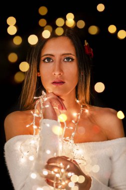 Genç bir kadın farklı pozlarda siyah bir arkaplanda Noel 'in sicim ışıklarını tutuyor..