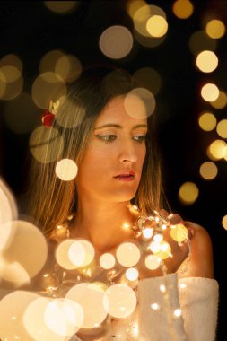 Genç bir kadın farklı pozlarda siyah bir arkaplanda Noel 'in sicim ışıklarını tutuyor..