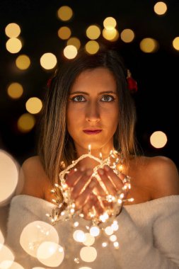 Genç bir kadın farklı pozlarda siyah bir arkaplanda Noel 'in sicim ışıklarını tutuyor..