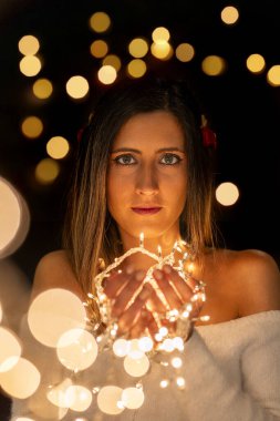 Genç bir kadın farklı pozlarda siyah bir arkaplanda Noel 'in sicim ışıklarını tutuyor..