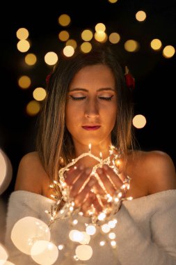 Genç bir kadın farklı pozlarda siyah bir arkaplanda Noel 'in sicim ışıklarını tutuyor..
