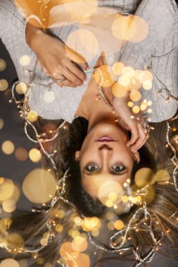 Genç bir kadın farklı pozlarda siyah bir arkaplanda Noel 'in sicim ışıklarını tutuyor..