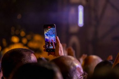 Canlı konser kaydetmek için modern bir cep telefonu kullanan bir hayranın yakın görüntüsü.