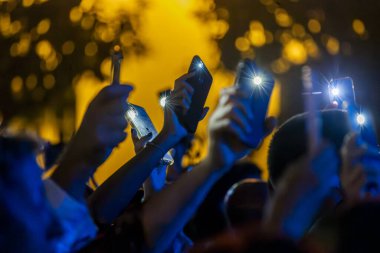Modern bir cep telefonuyla el feneriyle canlı bir konseri kaydeden hayranların yakın görüntüsü..