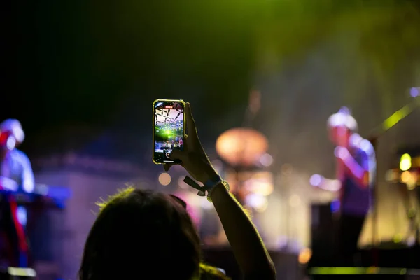 Close view of a fan using a modern cellphone to record a live concert.