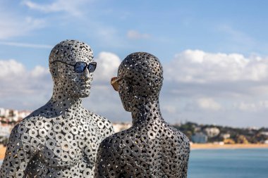 Albufeira şehrinde güneş gözlüğü takan bir adam ve kadının metal tüpler heykeli.