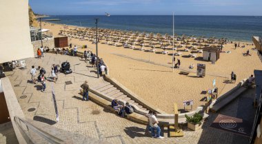 ALBUFEIRA, PORTUGAL - 7 Mayıs 2024: Portekiz 'in Albufeira plajındaki sazdan çatı şemsiyeleri ve şezlonglara erişim.