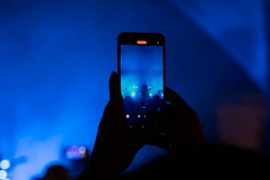 Müzik ve ışık gösterisi sırasında elinde akıllı telefon kayıtları tutan kişi.