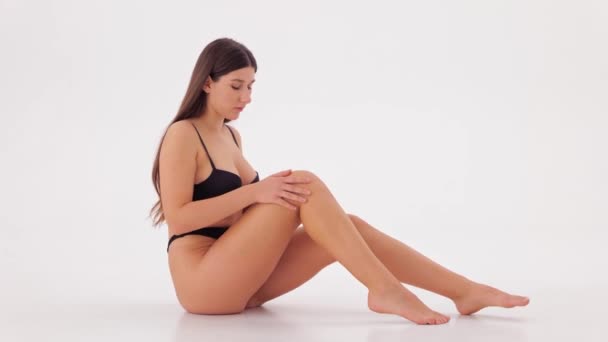 Νεαρή Όμορφη Γυναίκα Χαϊδεύει Απαλό Της Πόδι Καθισμένη Στο Λευκό — Αρχείο Βίντεο