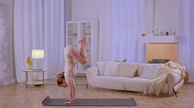 Atletik kız amuda kalkıyor ve evde yoga egzersizleri yapıyor. Yüksek kalite 4k görüntü