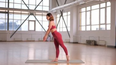 Büyük pencereli bir stüdyoda esneme hareketleri ve yoga egzersizleri yapan atletik bir kız. 3. Asana Savaşçısı Virabhadrasana C