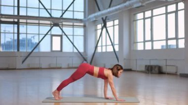 Büyük pencereli bir stüdyoda esneme hareketleri ve yoga egzersizleri yapan atletik bir kız. Tek bacaklı Plank Eka Pada Phalakasana