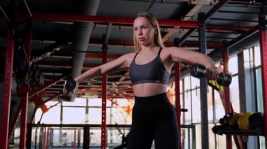  Kadın, kollarının ve omuzlarının kaslarını dambıllarla eğitir. Yan omuz dambılları kalkıyor. yavaş çekim