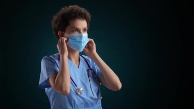 Mutlu Tıp Doktoru maskesini çıkarır ve siyah arka planda gülümser. Yüksek kalite 4k görüntü yavaş çekim