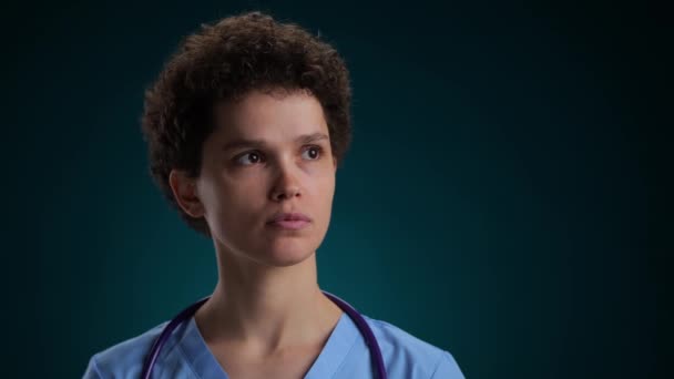若い医師の真面目な顔は 黒い背景に隠れている 高品質の4K映像 — ストック動画
