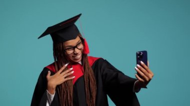 Siyah cüppeli mutlu Afrikalı kız ve usta şapkası bir telefondan video ile iletişim kuruyor. . 