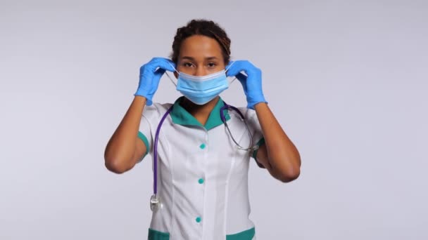 Feliz Enfermeira Médica Africana Coloca Uma Máscara Sorri Fundo Branco — Vídeo de Stock