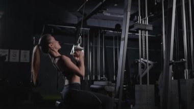 Bir kadın spor salonundaki bir makinede barfiks çekiyor, göğsünü, karnını, kalçasını ve dirsek kaslarını çalıştırıyor. Flaş fotoğrafçılık onun etkileyici güç ve atletizm gösterisini yakalıyor.