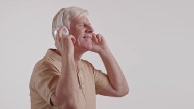 Yaşlı bir adam, çenesi ritme uygun hareket ederken başparmağı ve dirseğiyle hareketler yaparak kulaklıkla müzikten mutlu bir şekilde zevk alıyor. Kolundaki kurnaz yazı tipi onun neşeli ifadesine ekleniyor.