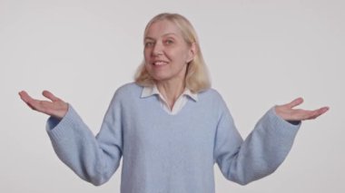 Mavi kazaklı bir kadın kollarını açmış, elleri tasmasının önünde bir jest yapıyor.