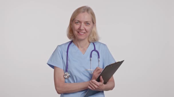 Γυναίκα Γιατρός Ηλεκτρικά Μπλε Γυαλιά Χαμογελά Κρατώντας Ένα Πρόχειρο Κάτω — Αρχείο Βίντεο