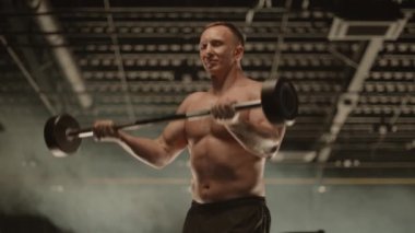 Bir müzisyen spor salonunda haltersiz bir halteri kaldırarak göğüs ve bacak kaslarını çalıştırıyor. Müzik performanslarında eğlenmek için güç ve dayanıklılık sağlıyor.