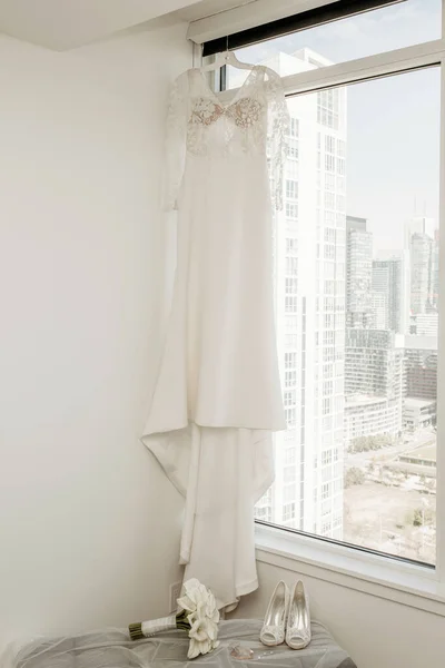 結婚式のドレス 花嫁の花束は 都市開発を背景にホテルの部屋の窓に掛けられています 結婚式の日と準備の花嫁のウェディングアクセサリー — ストック写真