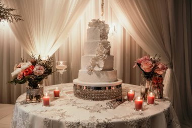 Çiçekler ve mumlarla süslenmiş bir restoranda güzel beyaz bir pasta. Restoranda bir masanın üzerinde düğün pastası yeni evliler tarafından kesilmek üzere hazırlanıyor. Pasta şeklinde tatlı.