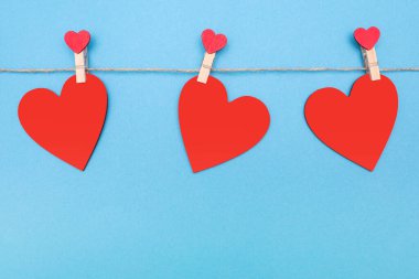 Mavi arka planda mandalları olan bir ipe bağlı üç kırmızı kalp var. Sevgililer Günü için kalp şeklinde güzel bir dekor ya da dekorasyon. Metin veya kopyalamak için boş alan
