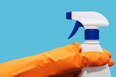 Plastik turuncu eldivenli bir insan eli mavi arka planda deterjan dolu bir sprey şişesi tutuyor. Pencereleri sprey şişede deterjanla temizleme ve yıkama kavramı.