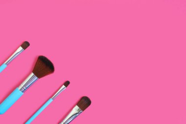 A set of four makeup brushes on a pink background. Four blue makeup brushes in different shapes and sizes. Fashionable female beauty tools for creating beauty. Free space for text