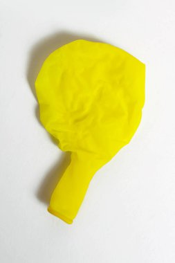 Deflated yellow balloon on a white isolated background. One uninflated balloon from above. The concept of the ended holidays in the form of a half-deflated yellow balloon
