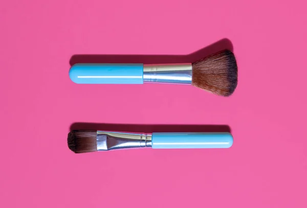 Cosmetic makeup brush on a pink background. Two blue makeup brushes of different sizes on a pink background. A fashionable tool for creating female beauty. Creative fashionable concept