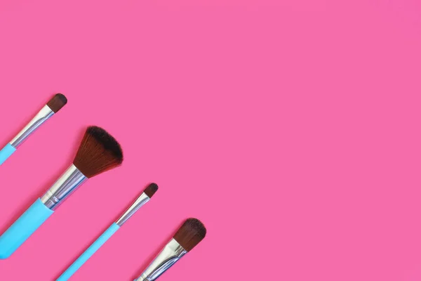 A set of four makeup brushes on a pink background. Four blue makeup brushes in different shapes and sizes. Fashionable female beauty tools for creating beauty. Free space for text