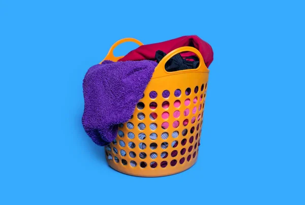 Dirty clothes are folded into a plastic orange laundry basket on a blue background. Housekeeping and laundry concept. Dirty clothes are placed in the basket and are ready for washing