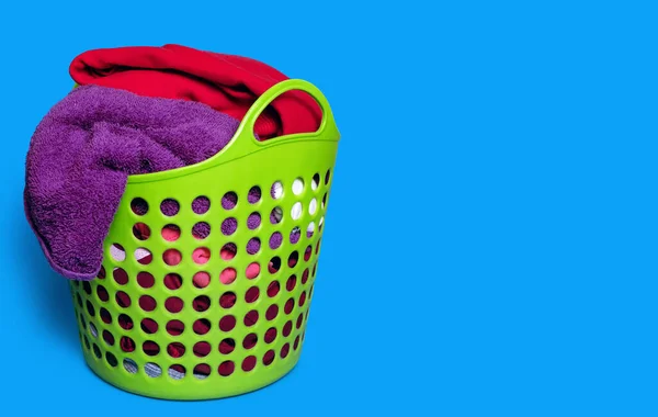 Dirty clothes in a plastic green laundry basket on a blue background. Housekeeping and laundry concept. Free space for text. Dirty clothes are placed in the basket and are ready to be washed