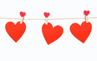 Three red hearts are attached to a rope with clothespins on a white background. Beautiful decor in the form of hearts or decoration for Valentine's Day. Three red hearts made of wood