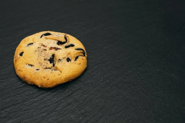 One chocolate chip cookie on a black background. Homemade chocolate chip cookies. Delicious pastries and a quick snack. Sweet dessert in the form of cookies with chocolate. Free space for text