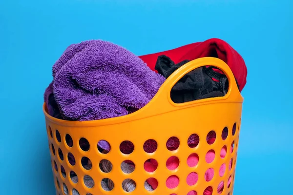 Dirty clothes are folded into a plastic orange laundry basket on a blue background close-up. Housekeeping and laundry concept. Dirty clothes are placed in the basket and are ready to be washed