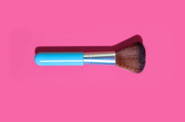 Cosmetic makeup brush on a pink background. One blue makeup brush on a pink background. Top view trendy feminine beauty tool in the form of a soft brush