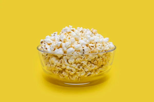 Popcorn in a large glass bowl on a yellow background. Crispy classic popcorn snack for watching movies and series. Delicious snack for spending free time and watching TV